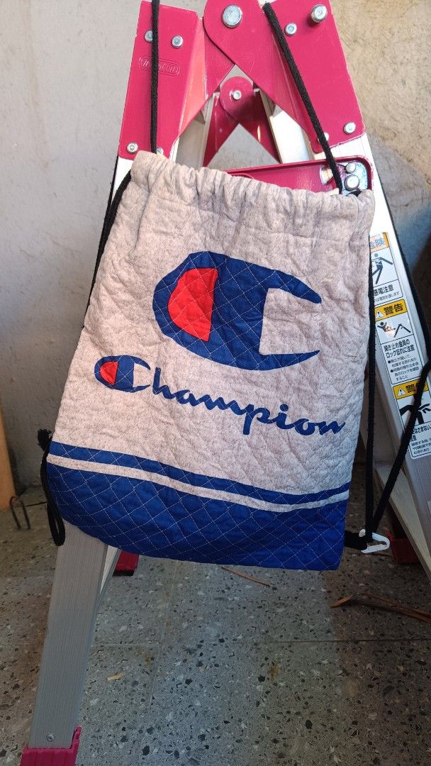 💯 Original Champion Quilted Drawstring Backpack Bag (Category: Backpacks) located in Cavite. Submitted by randzwurkz48441 (Listing ID 1470630559, Image 1). Description: - Brand: Champion - Dimensions: 15.5 x 12.5 inches - Type: Quilted drawstring bag - Color: Light Grey body with blue bottom panel and white accent stripes - Details: Classic red and blue Champion logo on the front - Straps: Durable black rope cords for shoulder wear - Condition: 