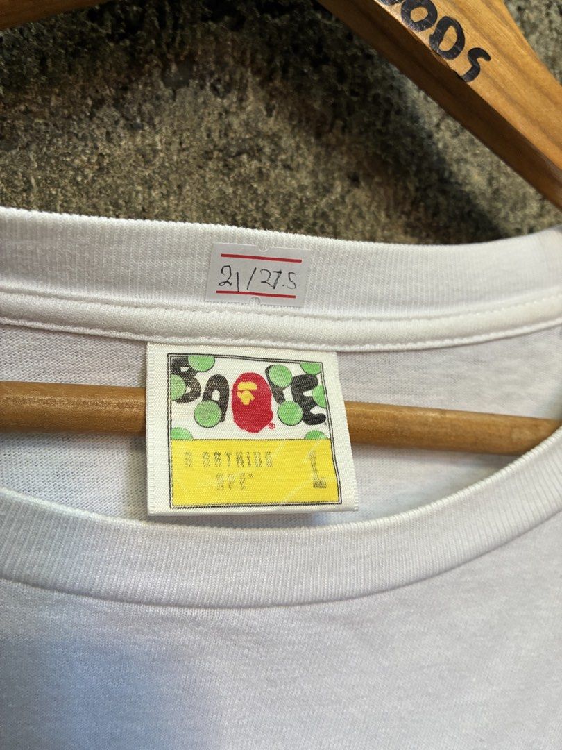 A Bathing Ape BAPE Multi Camo Logo T-Shirt White (Category: Tshirts & Polo Shirts ) located in Manila. Submitted by assortedgoodsv3 (Listing ID 1470620659, Image 3). Description: - Brand: A Bathing Ape (BAPE) - Item: White Graphic Tee - Size: Large - Design: Colorful camo print on chest with 'BY BATHING APE' lettering on the back hem - Details: Classic ape head logo tag on left sleeve cuff - Authenticity: Includes traditional yellow sizing label 