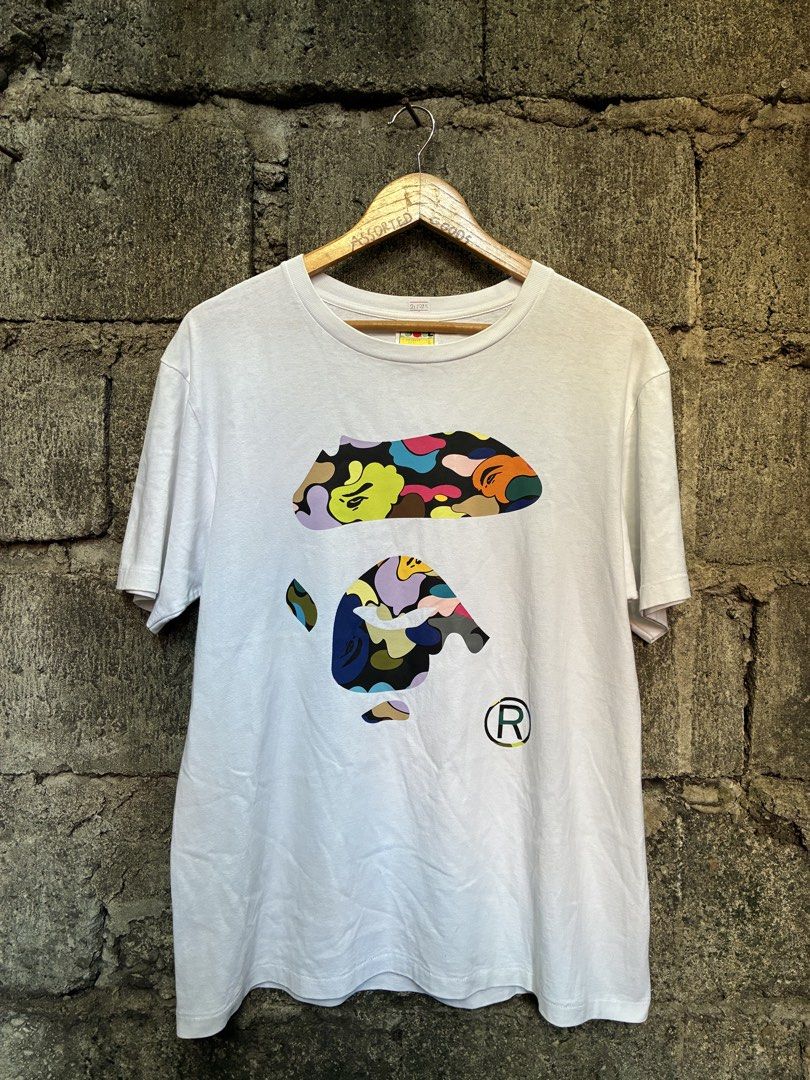 A Bathing Ape BAPE Multi Camo Logo T-Shirt White (Category: Tshirts & Polo Shirts ) located in Manila. Submitted by assortedgoodsv3 (Listing ID 1470620659, Image 1). Description: - Brand: A Bathing Ape (BAPE) - Item: White Graphic Tee - Size: Large - Design: Colorful camo print on chest with 'BY BATHING APE' lettering on the back hem - Details: Classic ape head logo tag on left sleeve cuff - Authenticity: Includes traditional yellow sizing label 