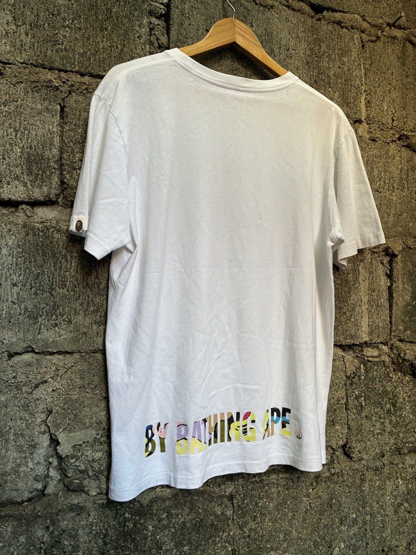 A Bathing Ape BAPE Multi Camo Logo T-Shirt White (Category: Tshirts & Polo Shirts ) located in Manila. Submitted by assortedgoodsv3 (Listing ID 1470620659, Image 2). Description: - Brand: A Bathing Ape (BAPE) - Item: White Graphic Tee - Size: Large - Design: Colorful camo print on chest with 'BY BATHING APE' lettering on the back hem - Details: Classic ape head logo tag on left sleeve cuff - Authenticity: Includes traditional yellow sizing label 