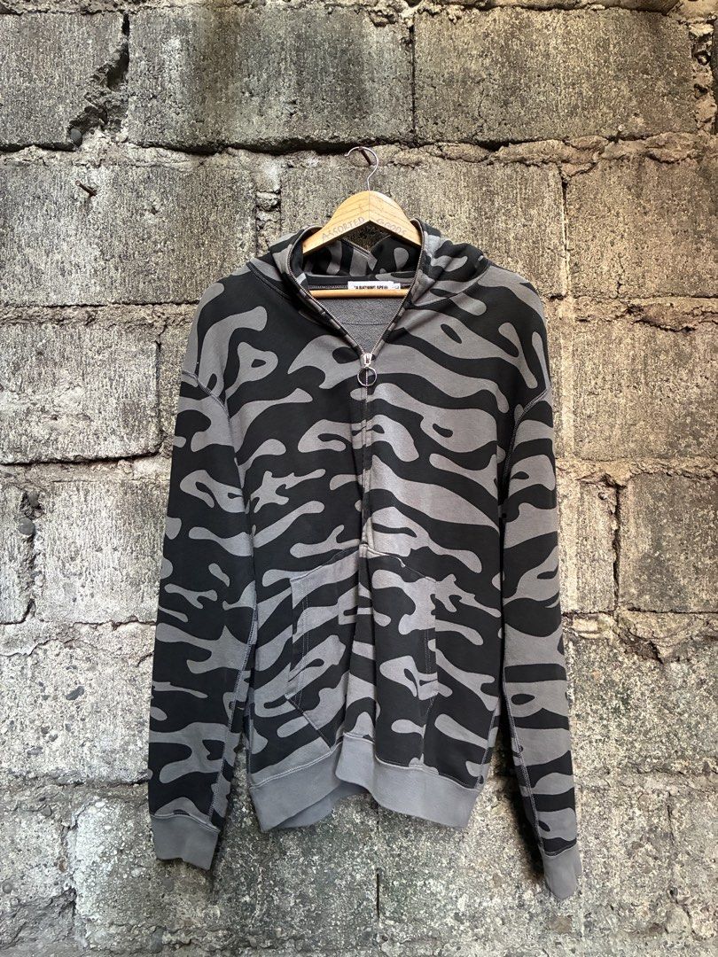 A Bathing Ape Camo Zip Up Hoodie (Category: Hoodies) located in Manila. Submitted by assortedgoodsv3 (Listing ID 1470619950, Image 2). Description: - Brand: A Bathing Ape (BAPE) - Design: Black and grey camo pattern with yellow hood graphics - Details: Ring pull zipper and front pockets - Back Graphic: Red and white text block lettering reading "A Bathing Ape in Lukewarm Water" - Fit: Ribbed cuffs and hem for comfort - Condition: Excellent, ready