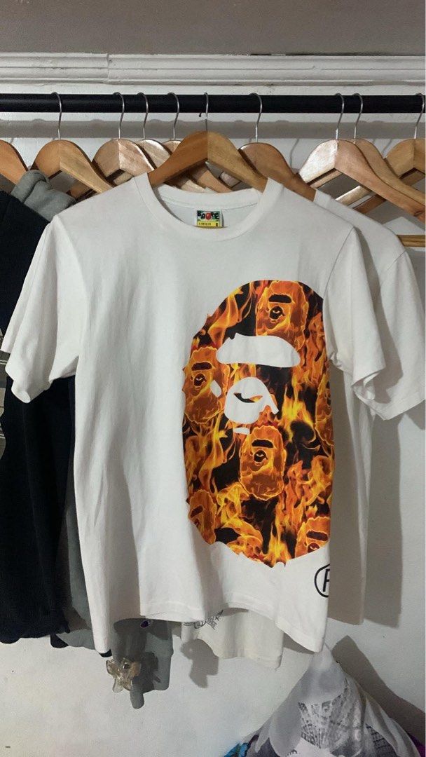 A Bathing Ape Fire Camo Ape Head T-shirt (Category: Tshirts & Polo Shirts ) located in Manila. Submitted by lstrthriftv1 (Listing ID 1470617683, Image 1). Description: - Brand: Bape - Item: Flaming Ape Head Tee - Color: White with vibrant fire print - Size: Small - Material: 100% cotton (Made in China) - Condition: Clean fabric, classic neck and sleeve tags intact - Ideal for streetwear styling.