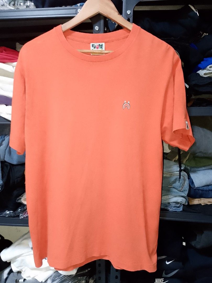 A Bathing Ape Shark Face Orange T-Shirt (Category: Tshirts & Polo Shirts ) located in Manila. Submitted by mjthrifted_second (Listing ID 1470614575, Image 1). Description: - Brand: A Bathing Ape (BAPE) - Color: Orange - Size: Medium -Dimes: 21/27 - Design: Small embroidered shark graphic on chest - Details: Classic sleeve tag near hem, printed neck label - Condition: Clean fabric, ready to wear.