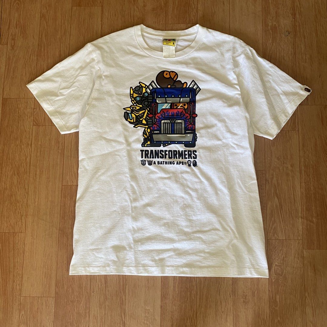 A Bathing Ape x Transformers White T-Shirt Size M (Category: Tshirts & Polo Shirts ) located in Manila. Submitted by 5treetw3ar (Listing ID 1470722942, Image 1). Description: - Brand: A Bathing Ape (BAPE) x Transformers - Color: White - Size: Medium (tag at collar intact) - Details: Features Optimus Prime, Bumblebee, and iconic Bape head logo with sleeve patch tag - Condition: Clean cotton fabric with vibrant chest print - Ideal for: Streetwear f