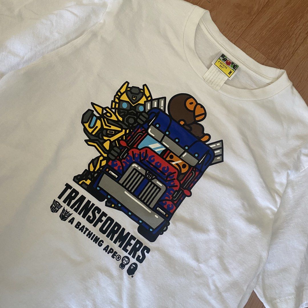 A Bathing Ape x Transformers White T-Shirt Size M (Category: Tshirts & Polo Shirts ) located in Manila. Submitted by 5treetw3ar (Listing ID 1470722942, Image 2). Description: - Brand: A Bathing Ape (BAPE) x Transformers - Color: White - Size: Medium (tag at collar intact) - Details: Features Optimus Prime, Bumblebee, and iconic Bape head logo with sleeve patch tag - Condition: Clean cotton fabric with vibrant chest print - Ideal for: Streetwear f