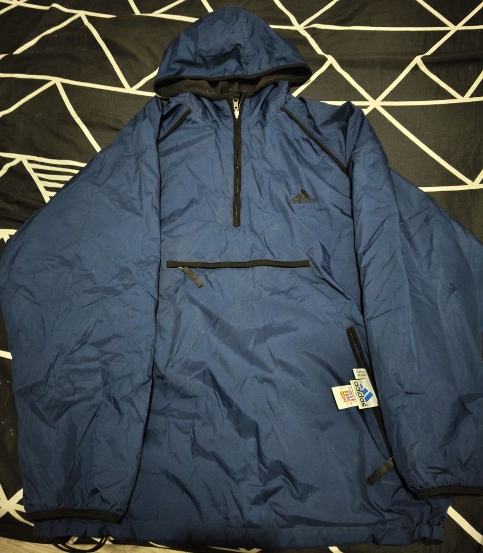 Adidas Blue Anorak Windbreaker Jacket (Category: Coats, Jackets and Outerwear) located in Bauang. Submitted by mr.acey (Listing ID 1470679752, Image 1). Description: - Authentic blue Adidas windbreaker with quarter zip and attached hood - Features a front kangaroo pocket and two secure side zippered pockets - Stylish dark blue contrast trim along seams and zipper paths - Classic embroidered Adidas logo on the upper chest - Lightweight shell mater
