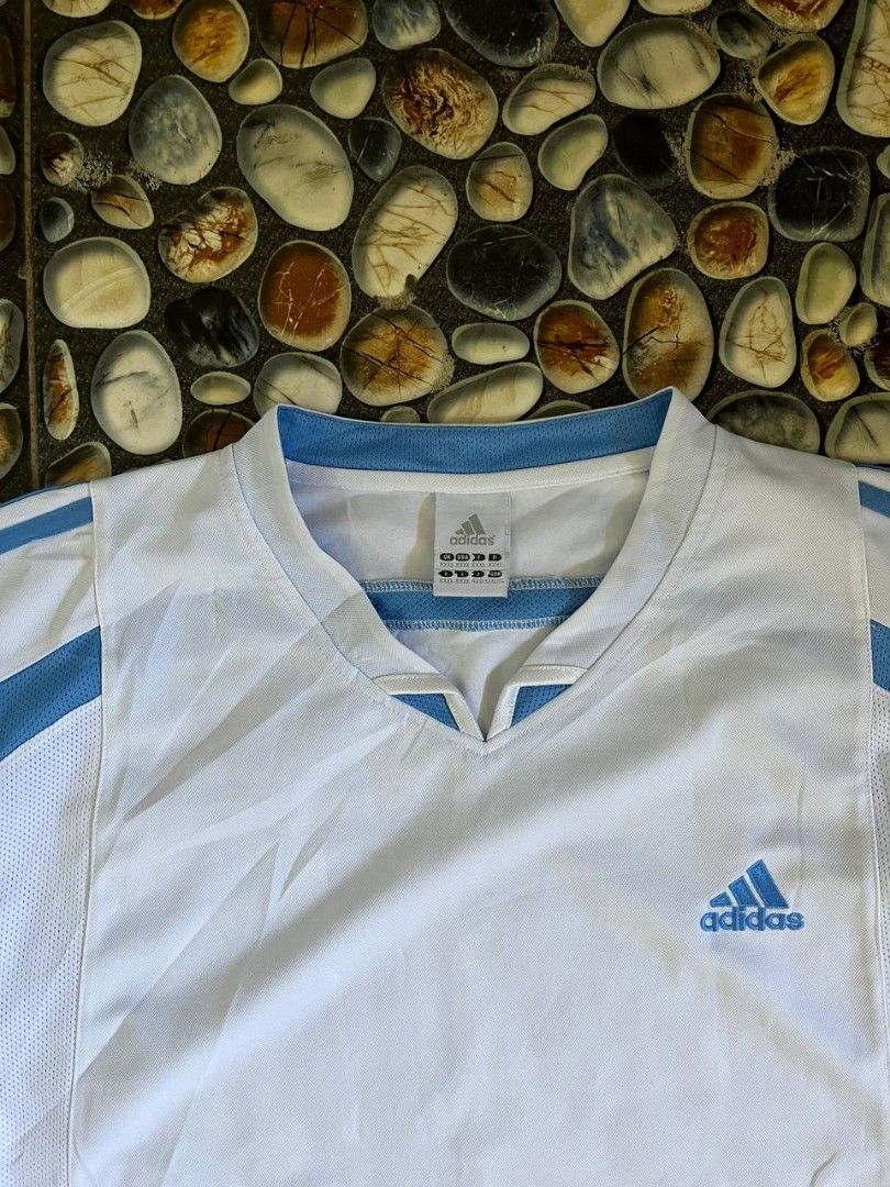 Adidas White Blue V-Neck Jersey (Category: Activewear) located in Baler. Submitted by vansonearth (Listing ID 1470701845, Image 3). Description: - Brand: Adidas - Color: White and blue with blue trim - Style: Classic retro sports jersey - Design: V-neck, short sleeves, and mesh panels on sides and shoulders - Branding: Embroidered blue Adidas logo on the chest - Size: XXL (multiple international sizing on tag) - Material: Breathable athletic fabr