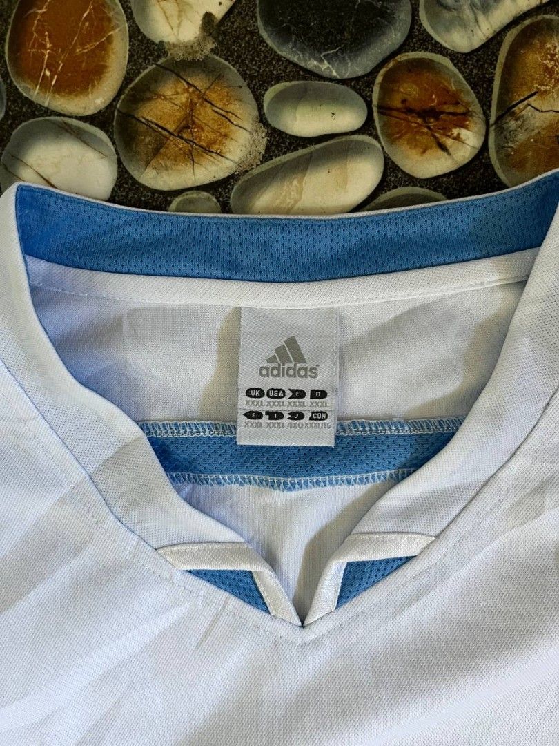 Adidas White Blue V-Neck Jersey (Category: Activewear) located in Baler. Submitted by vansonearth (Listing ID 1470701845, Image 2). Description: - Brand: Adidas - Color: White and blue with blue trim - Style: Classic retro sports jersey - Design: V-neck, short sleeves, and mesh panels on sides and shoulders - Branding: Embroidered blue Adidas logo on the chest - Size: XXL (multiple international sizing on tag) - Material: Breathable athletic fabr