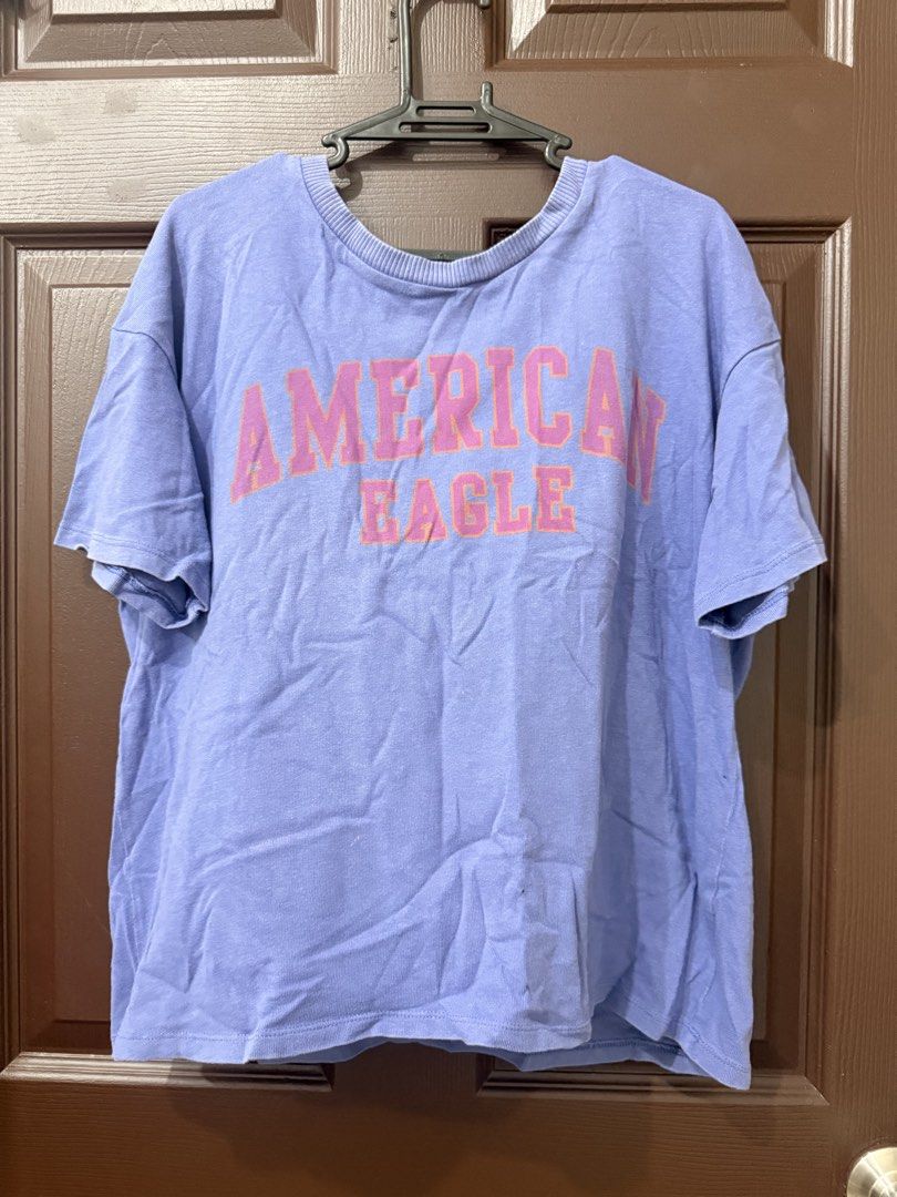American Eagle Light Purple Graphic T-Shirt (Category: Shirts) located in Pasay City. Submitted by annythingz28 (Listing ID 1470666325, Image 1). Description: - Brand: American Eagle - Color: Light purple with bold pink collegiate block lettering - Fit: Relaxed fit with a ribbed crew neck collar - Material: Soft and comfortable cotton - Condition: Worn a few times, excellent pre-loved condition.