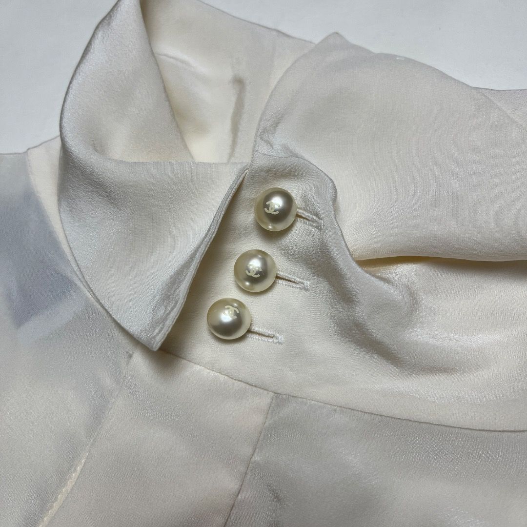 Authentic Chanel Silk Pearl Button Blouse Size 38 (Category: Luxury Apparel) located in Caloocan City. Submitted by achilles_grails (Listing ID 1470578450, Image 2). Description: - Brand: Chanel - Size: 38 (Medium) - Color: Classic White - Material: Lightweight, fluid silk with subtle vertical texture - Design: Long bishop sleeves, structured button cuffs, and classic pointed collar - Details: Signature pearl-effect CC logo buttons on the front p