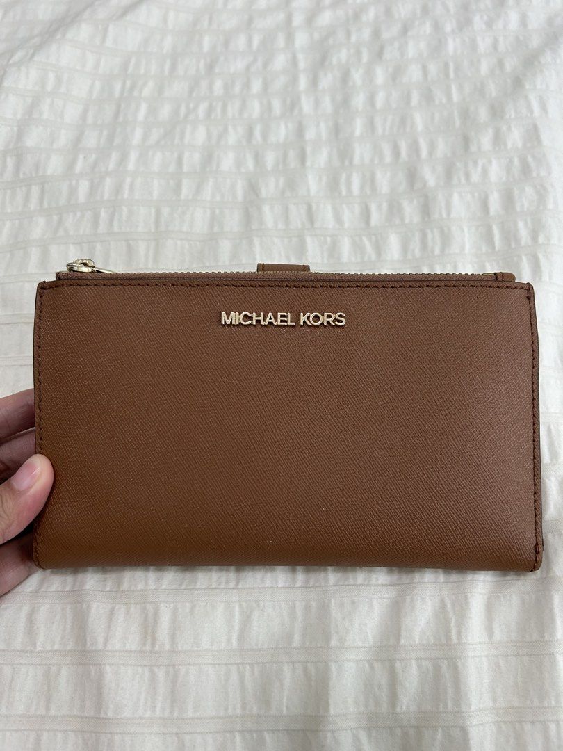 Authentic Michael Kors Jet Set Wallet ❤️ (Category: Wallets & Card holders) located in Taguig. Submitted by luckythriftph (Listing ID 1470586094, Image 1). Description: Selling my Michael Kors wallet in a beautiful, classic brown color with gold-tone hardware. ✨ Details: * Saffiano-textured leather * Elegant gold Michael Kors logo * Multiple card slots and ID window * Two zippered compartments * Spacious compartments for cash, receipts, and other