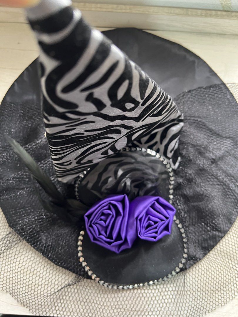 Black and silver zebra witch hat with purple roses (Category: Caps & Hats) located in Makati City. Submitted by esila.essentials (Listing ID 1470668924, Image 2). Description: FOR RENT - Design: Black and silver zebra print witch hat - Brim & Netting: Large black brim with layered black netting underneath - Details: Decorated with a sparkly sequin trim border and black feathers - Accents: Two vibrant bright purple satin roses near the front - Per
