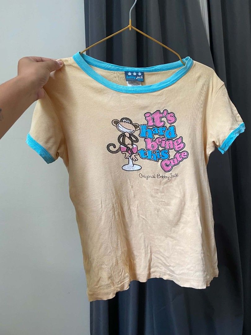 Bobby Jack Vintage Graphic Ringer T-Shirt (Category: Activewear) located in Malasiqui. Submitted by finnley26 (Listing ID 1470614883, Image 2). Description: - Authentic Bobby Jack ringer tee - Yellow body with light blue trim on collar and sleeves - Front graphic: Iconic monkey with "It's hard being this cute" text - Back graphic: Monkey covering mouth with "Not really hee hee hee" text - Retro Y2K style piece - Tagged original Bobby Jack brandin