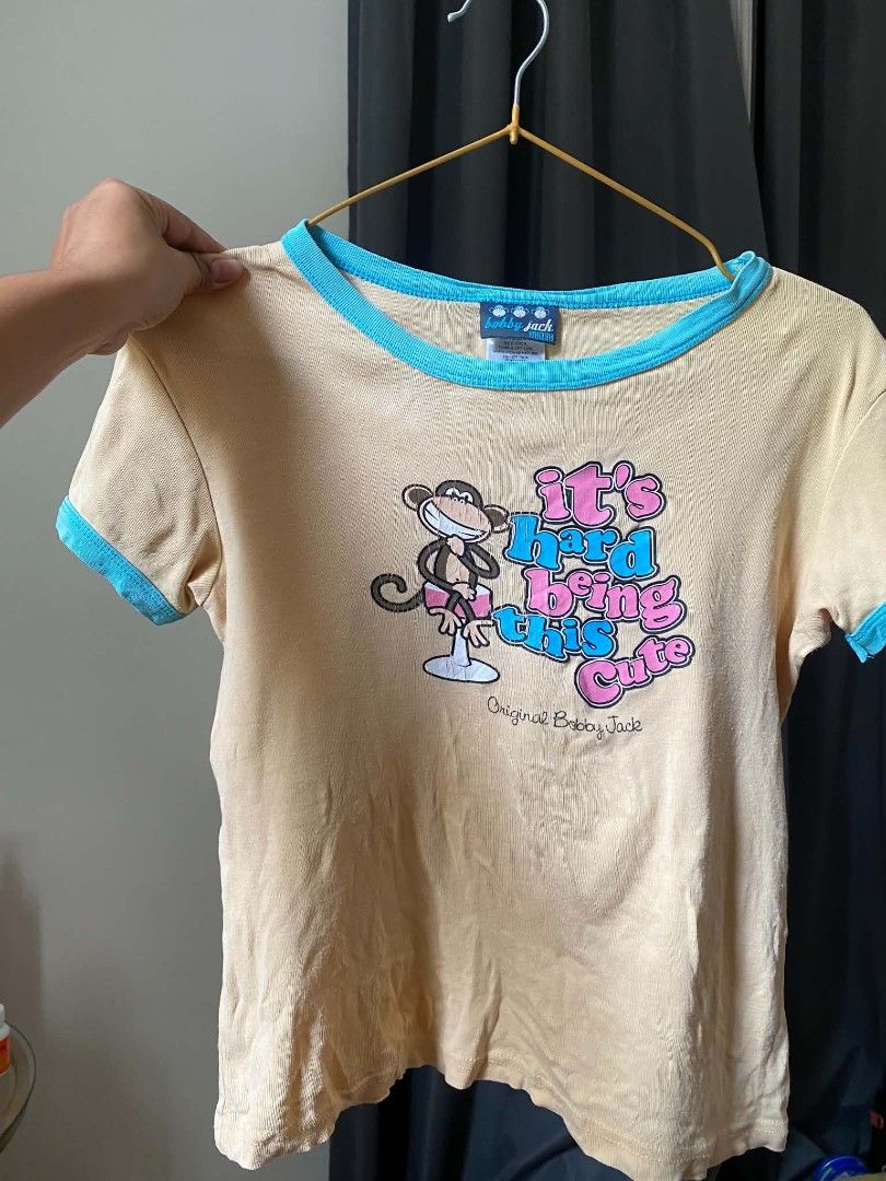 Bobby Jack Vintage Graphic Ringer T-Shirt (Category: Activewear) located in Malasiqui. Submitted by finnley26 (Listing ID 1470614883, Image 3). Description: - Authentic Bobby Jack ringer tee - Yellow body with light blue trim on collar and sleeves - Front graphic: Iconic monkey with "It's hard being this cute" text - Back graphic: Monkey covering mouth with "Not really hee hee hee" text - Retro Y2K style piece - Tagged original Bobby Jack brandin