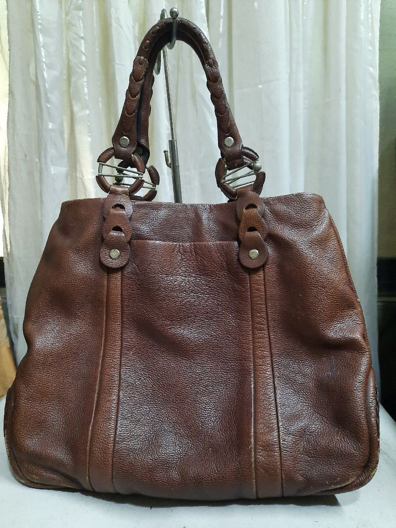 Braun Buffel brown leather tote bag (Category: Luxury Bags & Wallets) located in Quezon City. Submitted by dcmcentral (Listing ID 1470594506, Image 3). Description: - Brand: Braun Buffel - Color: Classic Brown - Material: Premium textured leather with structured depth - Handles: Stylish braided double handles with metal ring accents - Design: Vertical stitched panels and debossed brand logo - Functionality: Spacious interior with a reinforced bot