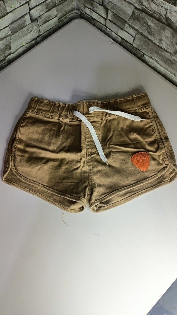 Brown casual shorts with drawstring and patch detail (Category: Shorts) located in Antipolo. Submitted by reahespiritu (Listing ID 1470619338, Image 1). Description: - Color: Brown - Material: Soft, comfortable fabric ideal for daily wear - Waistband: Elastic with an adjustable white drawstring - Design details: Small orange patch on the left leg and two back pockets with flap closures - Cut: Short length with a stylish curved hem.