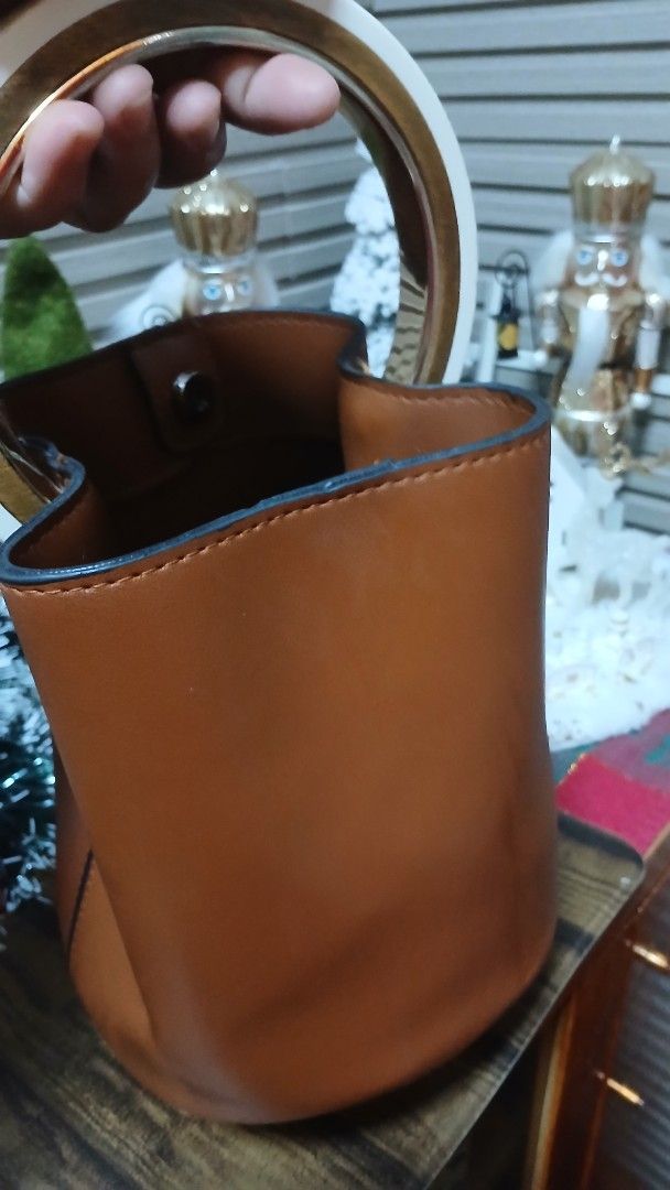 Brown Leather Bucket Bag with Circular Handle (Category: Luxury Bags & Wallets) located in Taguig. Submitted by jegadablo (Listing ID 1470741315, Image 3). Description: - Color & Material: Tan brown leather bucket bag - Handle: Circular top handle with stylish white and gold contrast - Base: Structured base equipped with four metal protective feet - Closure: Secure magnetic snap button at the top - Interior: Unlined with a spacious single compart