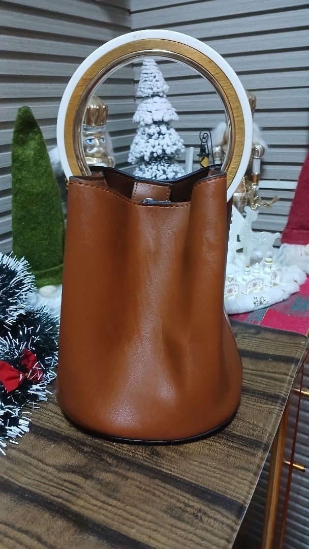 Brown Leather Bucket Bag with Circular Handle (Category: Luxury Bags & Wallets) located in Taguig. Submitted by jegadablo (Listing ID 1470741315, Image 2). Description: - Color & Material: Tan brown leather bucket bag - Handle: Circular top handle with stylish white and gold contrast - Base: Structured base equipped with four metal protective feet - Closure: Secure magnetic snap button at the top - Interior: Unlined with a spacious single compart