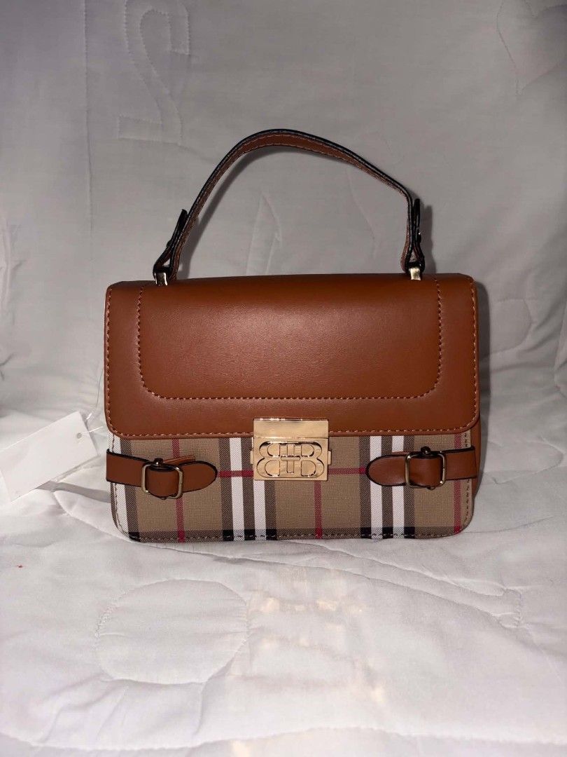 BURBERRY CROSSBODY BAG (Category: Luxury Bags & Wallets) located in Manila. Submitted by jcyle (Listing ID 1470715712, Image 1). Description: - Brand new with price tag still attached - Stylish brown faux leather with a classic tartan check pattern - Elegant gold-tone center clasp closure and decorative buckle straps - Convenient single top handle with gold hardware - Compact structured design with a flat base for easy storage.