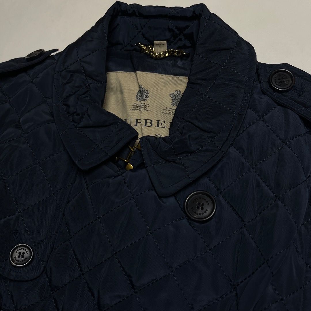 Burberry Quilted Nylon Trench Coat (Category: Coats, Jackets and Outerwear) located in Caloocan City. Submitted by achilles_grails (Listing ID 1470592994, Image 2). Description: - Brand: Burberry - Style: Quilted Nylon Trench Coat / Double-Breasted Jacket - Color: Dark Navy Blue - Size: XL (185/104B) - Material: 100% Polyester outer shell, 100% Viscose lining - Features: Diamond-quilted pattern, matching waist belt, shoulder epaulettes, branded b