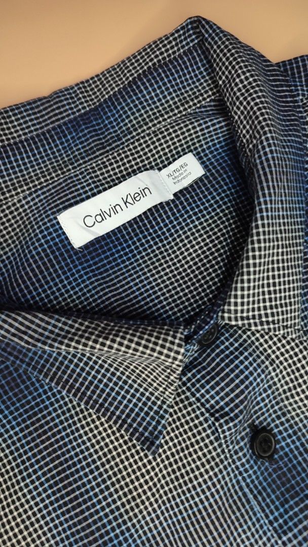Calvin Klein Blue Checked Short Sleeve Shirt (Category: Tshirts & Polo Shirts ) located in Cavite. Submitted by juanpraktikal (Listing ID 1470738112, Image 3). Description: - Brand: Calvin Klein - Size: XL 25" x 30.5" Length - Color/Pattern: Blue and grey checked - Material: 97% cotton, 3% elastane blend (slight stretch) - Details: Regular button-down closure, dark buttons, classic collar, chest pocket with small embroidered ck logo - Condition: 