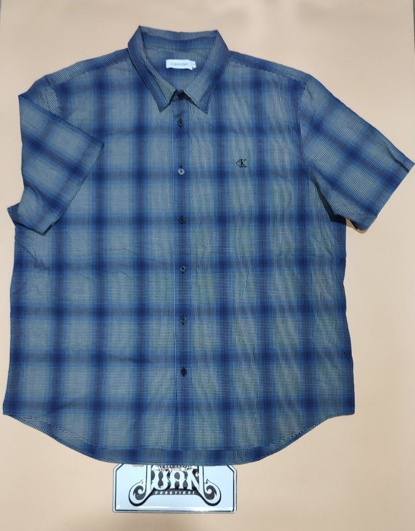 Calvin Klein Blue Checked Short Sleeve Shirt (Category: Tshirts & Polo Shirts ) located in Cavite. Submitted by juanpraktikal (Listing ID 1470738112, Image 1). Description: - Brand: Calvin Klein - Size: XL 25" x 30.5" Length - Color/Pattern: Blue and grey checked - Material: 97% cotton, 3% elastane blend (slight stretch) - Details: Regular button-down closure, dark buttons, classic collar, chest pocket with small embroidered ck logo - Condition: 