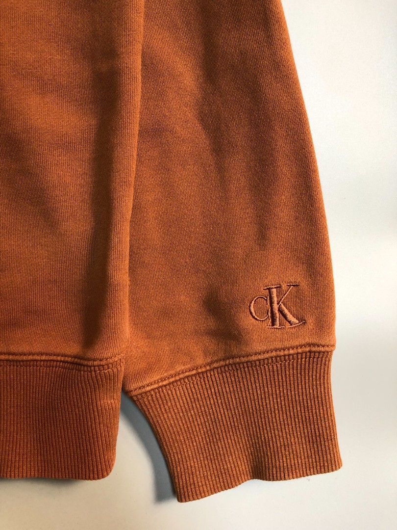 Calvin Klein Jeans Embossed Monogram Sweatshirt (Category: Coats, Jackets and Outerwear) located in Manila. Submitted by silentwolf_3303a7 (Listing ID 1470559455, Image 3). Description: * Color: Warm Brown / Copper * Size: Large (27.5" Length x 22.5" Width) * Condition: 7/10 (Good vintage condition) * Details: Raised metallic CK logo on chest + embroidered logo on wrist. May minimal print cracking for that vintage distressed aesthetic. .