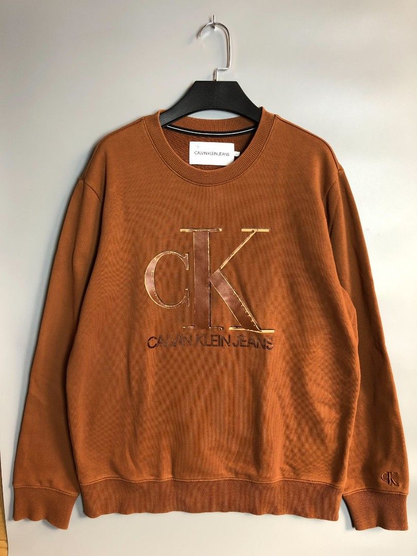 Calvin Klein Jeans Embossed Monogram Sweatshirt (Category: Coats, Jackets and Outerwear) located in Manila. Submitted by silentwolf_3303a7 (Listing ID 1470559455, Image 1). Description: * Color: Warm Brown / Copper * Size: Large (27.5" Length x 22.5" Width) * Condition: 7/10 (Good vintage condition) * Details: Raised metallic CK logo on chest + embroidered logo on wrist. May minimal print cracking for that vintage distressed aesthetic. .