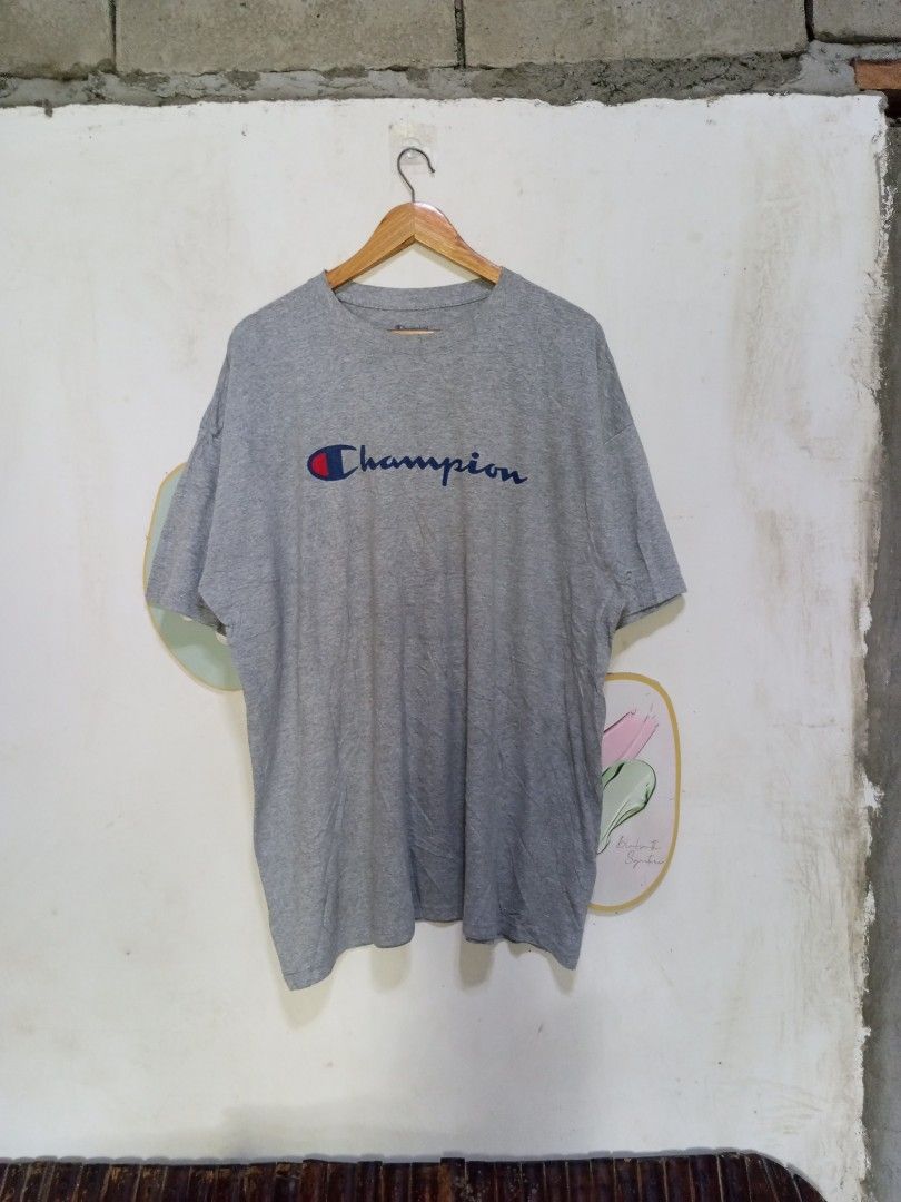 Champion Script Logo Grey T-Shirt 2XL (Category: Tshirts & Polo Shirts ) located in Magdalena. Submitted by magdalenathrift20 (Listing ID 1470671910, Image 2). Description: - Brand: Champion - Color: Grey - Size: 2XL (Width: 27", Length: 31") - Material: 100% cotton, made in Honduras - Condition/Details: Authentic athleticwear with classic crewneck and printed chest script logo.