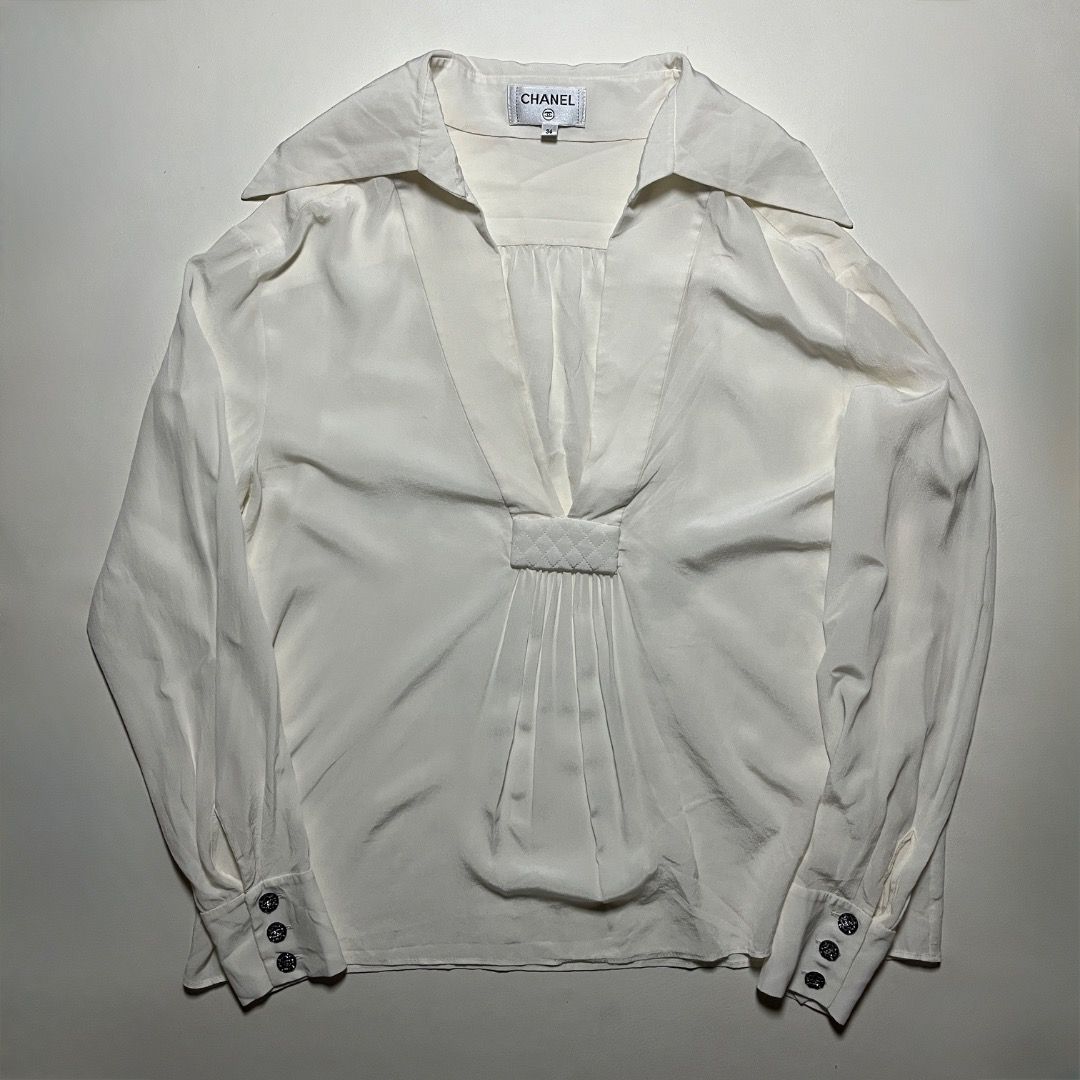 Chanel White Silk Blouse (Category: Blouses) located in Caloocan City. Submitted by achilles_grails (Listing ID 1470727553, Image 1). Description: - - Size: 36 (PH Small to Medium) - Chic pointed collar with deep V-neckline - Elegant pleated front panel with stitched quilted tab detail - Long sleeves featuring 3 dark patterned buttons on each cuff - Classic Chanel brand label inside neckline - Premium silk material, luxurious feel - Perfect for f