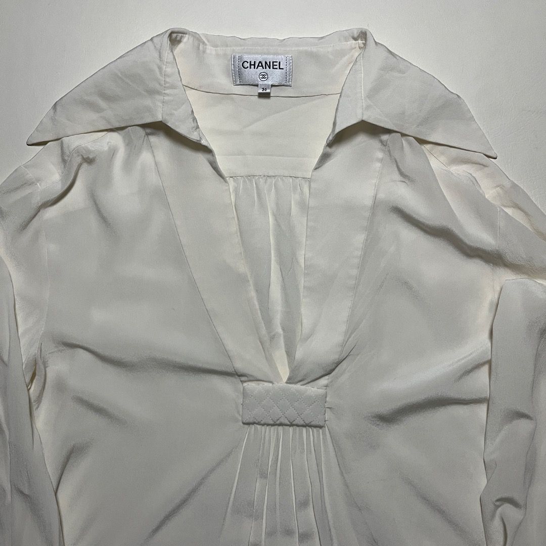 Chanel White Silk Blouse (Category: Blouses) located in Caloocan City. Submitted by achilles_grails (Listing ID 1470727553, Image 2). Description: - - Size: 36 (PH Small to Medium) - Chic pointed collar with deep V-neckline - Elegant pleated front panel with stitched quilted tab detail - Long sleeves featuring 3 dark patterned buttons on each cuff - Classic Chanel brand label inside neckline - Premium silk material, luxurious feel - Perfect for f
