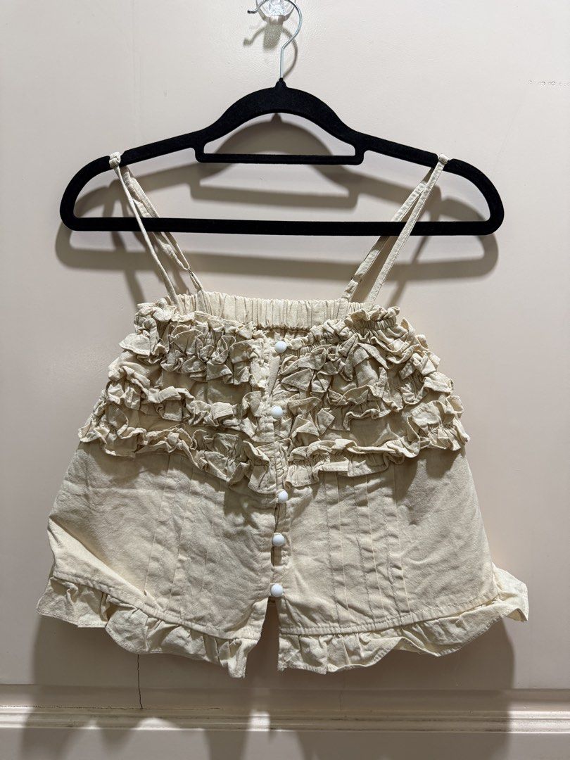 Cream Ruffle Cami Top with Buttons (Category: Sleeveless) located in Davao. Submitted by 2ndbase.dvo.ii (Listing ID 1470596297, Image 2). Description: - Color: Cream - Style: Cottagecore / Coquette - Details: Ruffled chest and hem, pleated lower front, round white buttons - Straps: Adjustable thin shoulder straps - Closure: Button-down front - Fabric: Light and breathable, ideal for warmer weather - Condition: Excellent, no major flaws noticed.