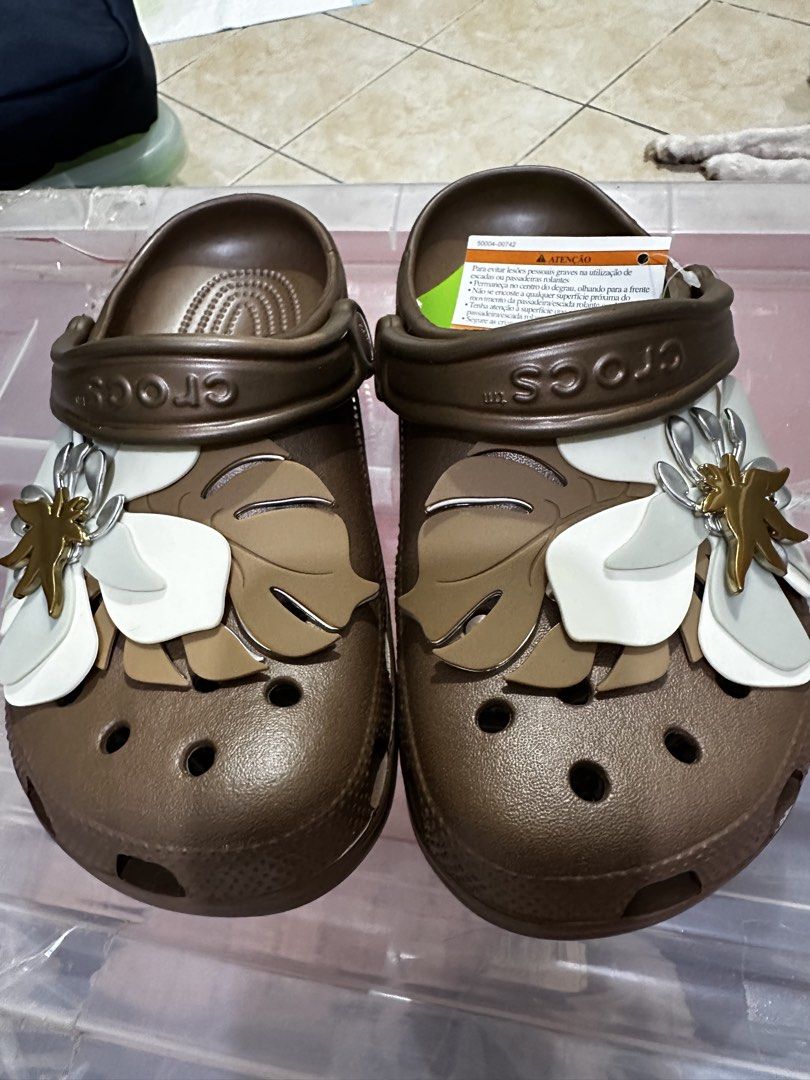 Crocs Brown Floral Clogs (Category: Slippers and slides) located in Balanga. Submitted by jamilbeauty5 (Listing ID 1470597950, Image 2). Description: - Brand new brown Crocs clogs in slip-on style - Decorated with trendy white floral and monstera leaf charms - Features ventilation holes on the toe box for breathability - Adjustable brown pivoting heel strap with Crocs branding - Comes with original product tag and plastic protective wrapping - Gu