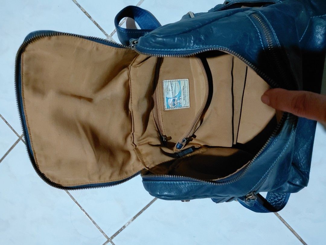 Design by Kang Jung Hee blue leather backpack (Category: Backpacks) located in Bacolod City. Submitted by cano47 (Listing ID 1470684837, Image 3). Description: - Brand/Designer: Design by Kang Jung Hee - Color: Dark blue - Material: Soft wrinkled leather with brass hardware and adjustable blue fabric straps - Compartments: Front exterior zip pocket, main zip compartment, and top grab handle - Interior: Beige fabric lining with an extra zip pocket
