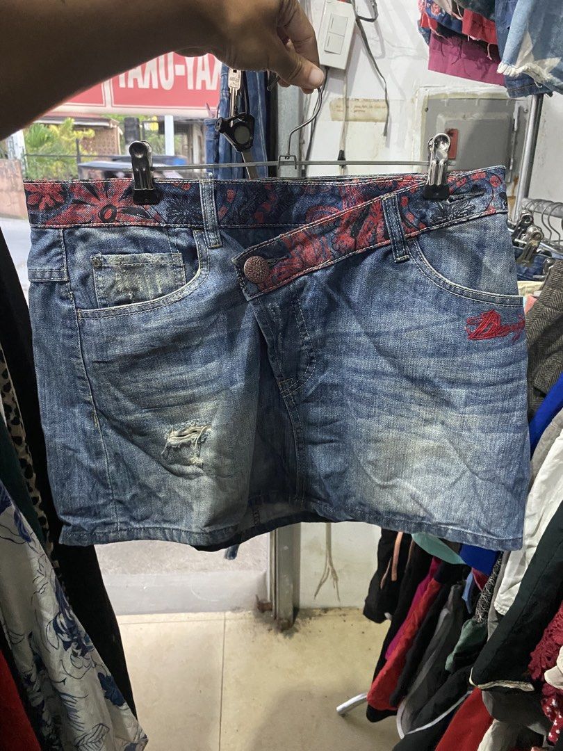 Desigual Denim Skirt Size 38 (Category: Skirts) located in Bulacan. Submitted by _myarchive (Listing ID 1470569548, Image 1). Description: - Brand: Desigual - Type: Denim Skirt - Size: 38 - Color: Blue with red patterned waistband - Closure: Asymmetrical button fly - Details: Distressed front, red embroidered logo on the front pocket - Back: Asymmetrical pockets with colorful embroidered detailing.