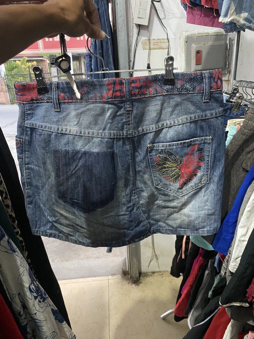 Desigual Denim Skirt Size 38 (Category: Skirts) located in Bulacan. Submitted by _myarchive (Listing ID 1470569548, Image 2). Description: - Brand: Desigual - Type: Denim Skirt - Size: 38 - Color: Blue with red patterned waistband - Closure: Asymmetrical button fly - Details: Distressed front, red embroidered logo on the front pocket - Back: Asymmetrical pockets with colorful embroidered detailing.