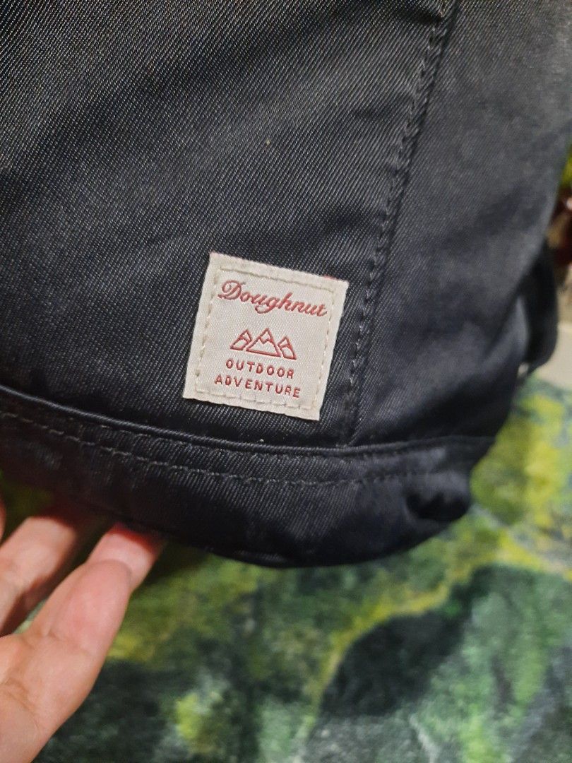 Doughnut Outdoor Adventure Black Backpack (Category: Backpacks) located in Baguio. Submitted by klayblakeb87803 (Listing ID 1470658554, Image 2). Description: - Brand: Doughnut Outdoor Adventure - Color: Solid black with tan inner lining - Dimensions: 11" height x 9" base - Closure: Flap top with buckle & secure drawstring main compartment - Pockets: Dual front snap pockets - Straps: Adjustable shoulder straps - Condition: Excellent / Well-mainta
