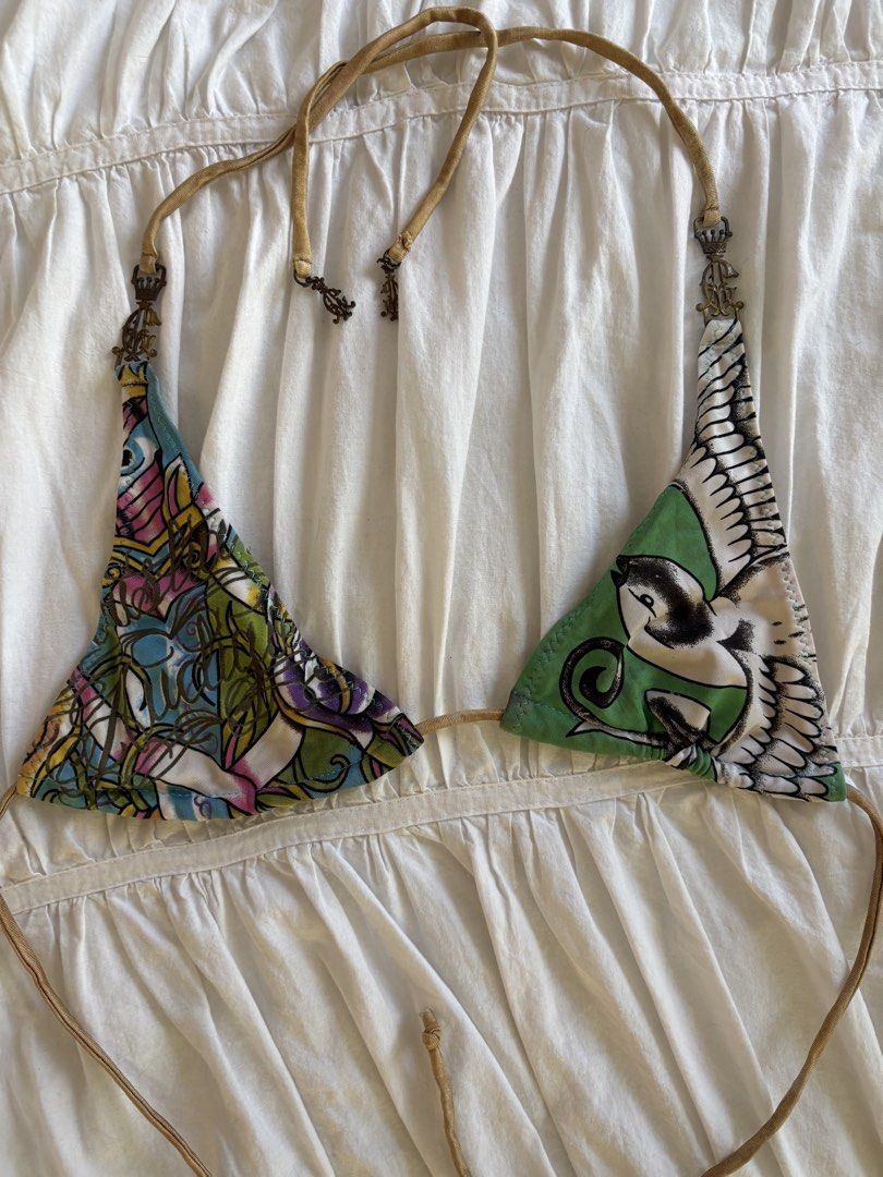 Ed Hardy Mismatch Halter Bikini Top Y2K (Category: Bikinis & Swimsuits) located in Makati City. Submitted by audrey.hepburn (Listing ID 1470633341, Image 2). Description: - Brand: Ed Hardy - Style: Halter bikini top with unique mismatched cups - Design: Multicolor tattoo graphics on one side, bird graphic on green on the other - Details: Tan straps accented with ornate crown hardware charms - Closure: Adjustable tie closure at neck and back - Con