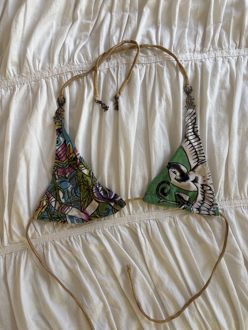 Ed Hardy Mismatch Halter Bikini Top Y2K (Category: Bikinis & Swimsuits) located in Makati City. Submitted by audrey.hepburn (Listing ID 1470633341, Image 1). Description: - Brand: Ed Hardy - Style: Halter bikini top with unique mismatched cups - Design: Multicolor tattoo graphics on one side, bird graphic on green on the other - Details: Tan straps accented with ornate crown hardware charms - Closure: Adjustable tie closure at neck and back - Con