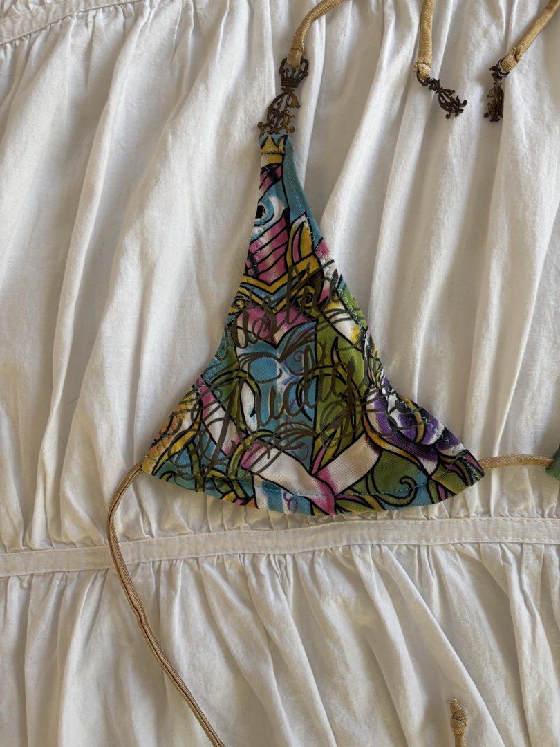 Ed Hardy Mismatch Halter Bikini Top Y2K (Category: Bikinis & Swimsuits) located in Makati City. Submitted by audrey.hepburn (Listing ID 1470633341, Image 3). Description: - Brand: Ed Hardy - Style: Halter bikini top with unique mismatched cups - Design: Multicolor tattoo graphics on one side, bird graphic on green on the other - Details: Tan straps accented with ornate crown hardware charms - Closure: Adjustable tie closure at neck and back - Con