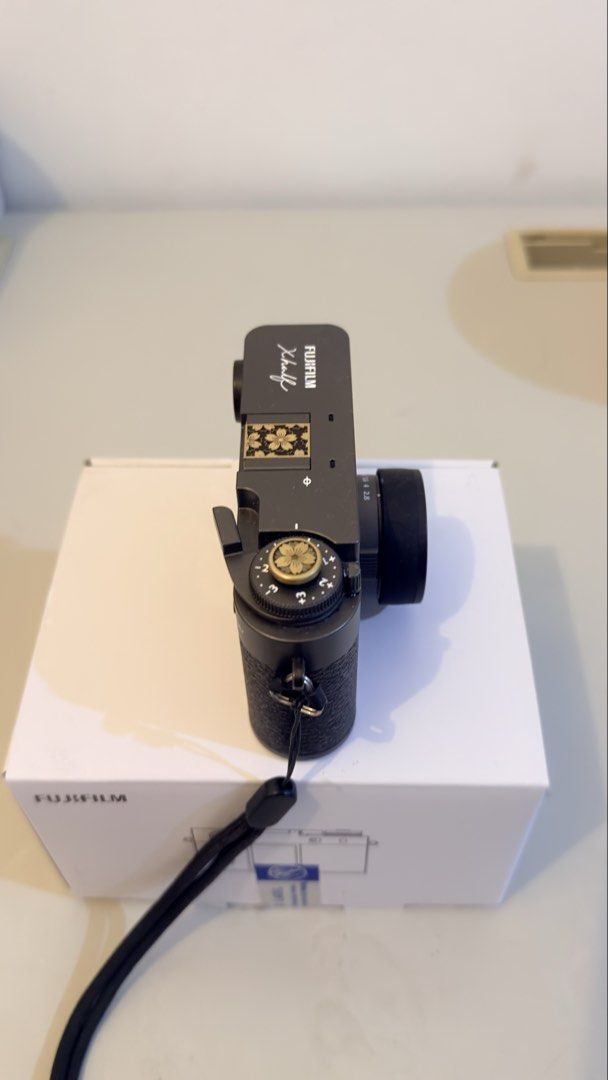 Fujifilm Xhalf Digital Camera with Box and Strap (Category: Cameras) located in Santa Maria. Submitted by jestonicruz (Listing ID 1470661872, Image 2). Description: - Model: Fujifilm Xhalf Digital Camera (Black) - Condition: Clean exterior finish, excellent ready-to-use condition - Inclusions: Original white box, lens cap, and attached black neck strap - Customizations: Decorative floral cover on the hot shoe mount and matching floral shutter but