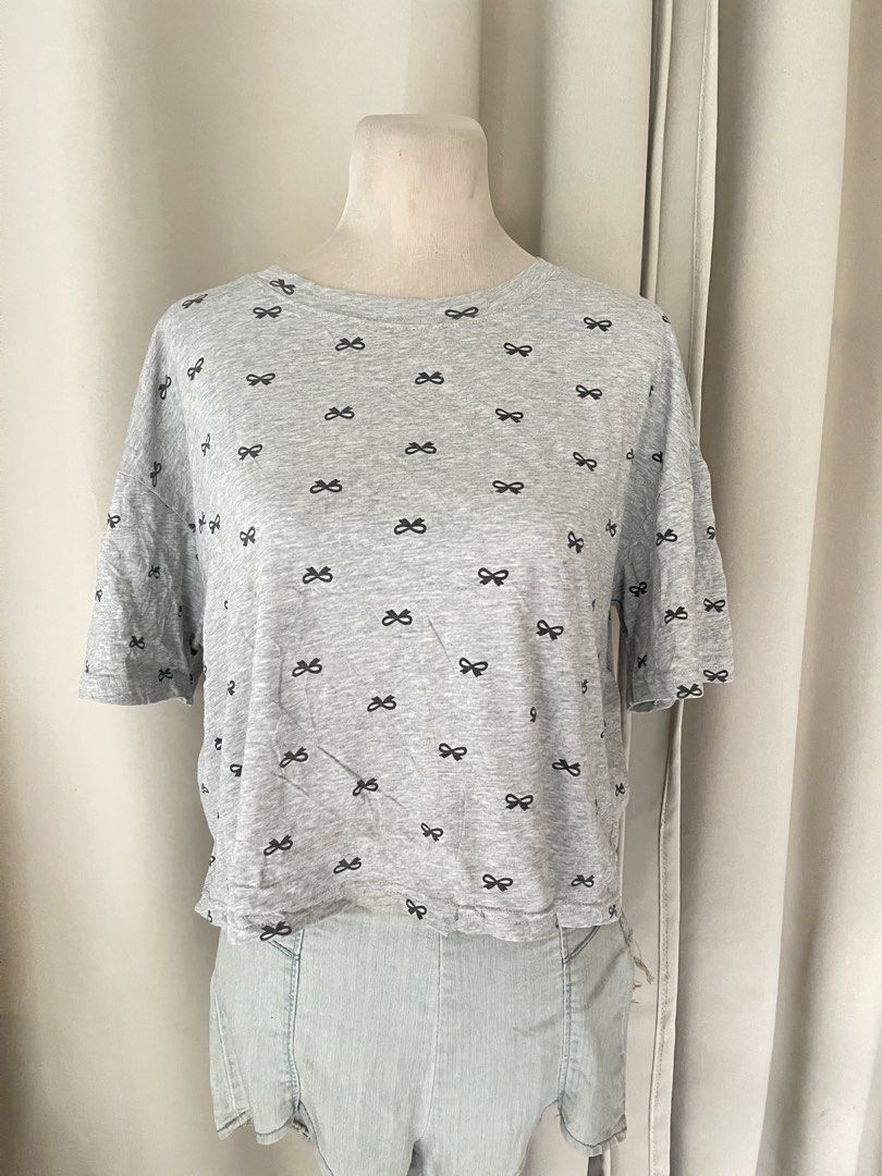 Grey Bow Print crop tee (Category: Shirts) located in Cainta. Submitted by zlove111 (Listing ID 1470704486, Image 1). Description: - Color & Pattern: Grey with all-over small black bow print - Fit: Crew neckline, relaxed fit with slightly dropped shoulders - Material: Lightweight cotton blend - Condition: Good, but has a small tear near the bottom front hem (refer to the 2nd photo for details) - Style: Perfect for easy, casual everyday outfits up