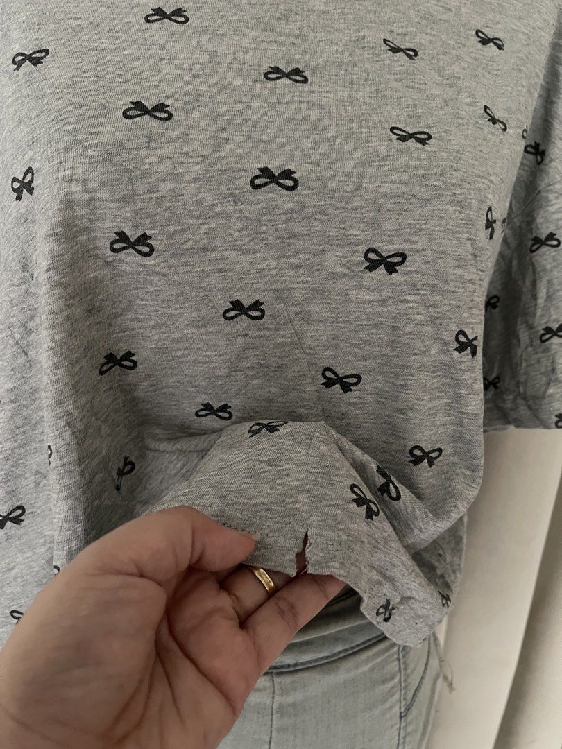Grey Bow Print crop tee (Category: Shirts) located in Cainta. Submitted by zlove111 (Listing ID 1470704486, Image 2). Description: - Color & Pattern: Grey with all-over small black bow print - Fit: Crew neckline, relaxed fit with slightly dropped shoulders - Material: Lightweight cotton blend - Condition: Good, but has a small tear near the bottom front hem (refer to the 2nd photo for details) - Style: Perfect for easy, casual everyday outfits up