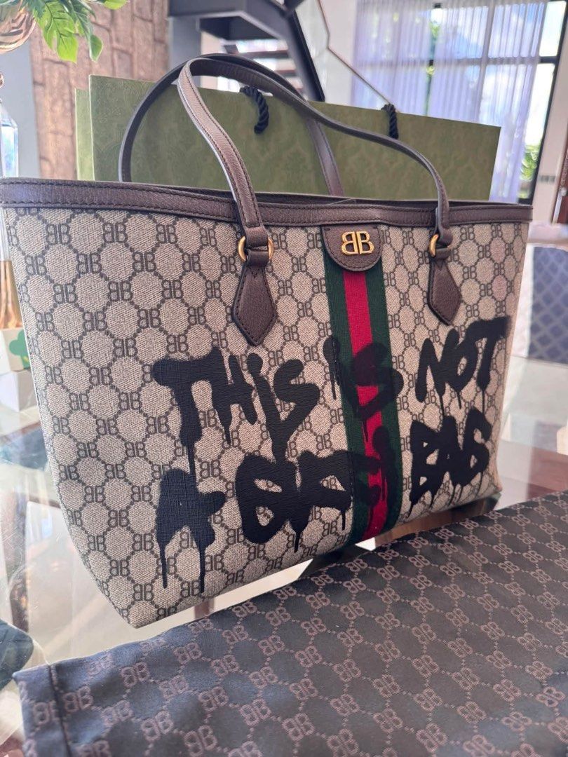 Gucci x Balenciaga Hacker Project Medium Graffiti Tote Bag (Category: Tote Bags) located in Quezon City. Submitted by jingjing93 (Listing ID 1470660289, Image 2). Description: - Authentic UNUSED Gucci x Balenciaga Hacker Project medium graffiti tote - Beige monogram jacquard canvas with BB print and signature green-red-green web stripe - Features bold black spray paint graffiti 'This Is Not A Gucci Bag' across the front - Premium brown leather tr