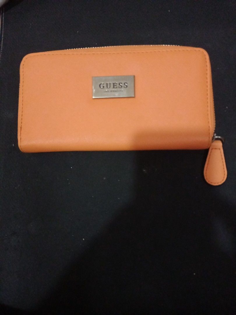 Guess Orange Zip Around Long Wallet (Category: Wallets & Card holders) located in Manila. Submitted by luckyeagle-7ff8 (Listing ID 1470589114, Image 1). Description: - Brand: Guess - Color: Bright orange with light beige interior - Closure: Smooth zip-around with matching pull tab - Exterior: Metal logo plate on the front - Interior: Multiple card slots, slip compartments, and a middle zippered coin pocket - Condition: Clean inside and out, excel