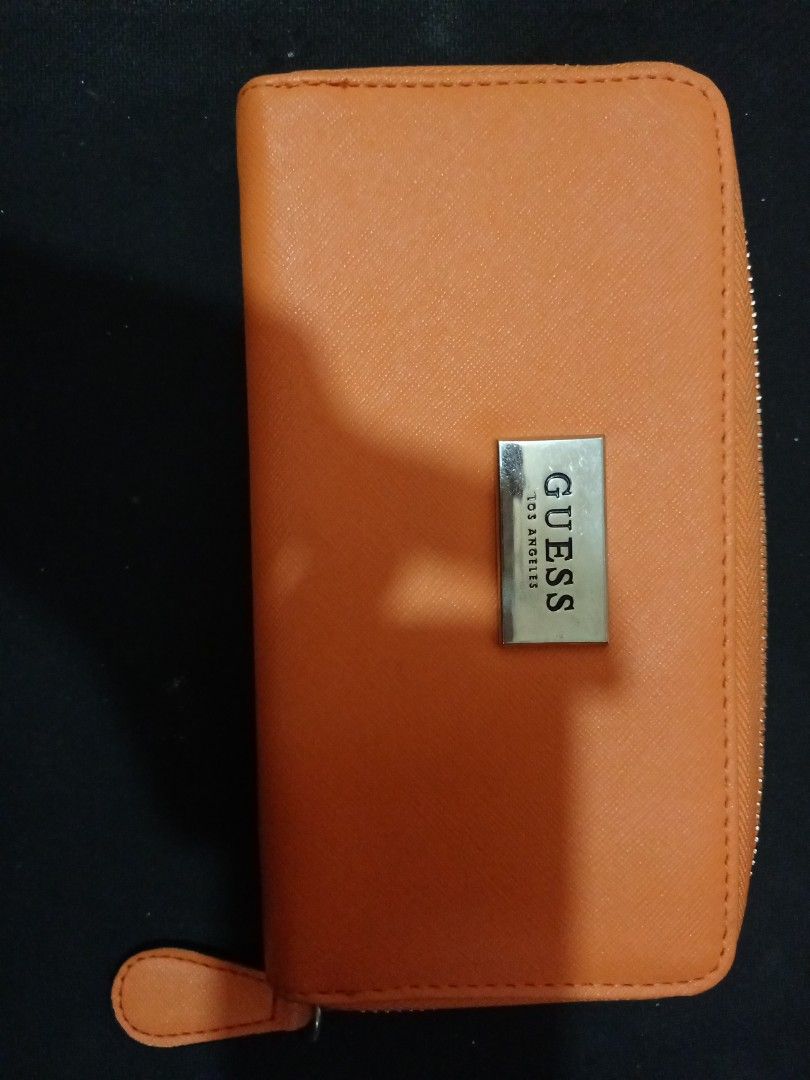 Guess Orange Zip Around Long Wallet (Category: Wallets & Card holders) located in Manila. Submitted by luckyeagle-7ff8 (Listing ID 1470589114, Image 2). Description: - Brand: Guess - Color: Bright orange with light beige interior - Closure: Smooth zip-around with matching pull tab - Exterior: Metal logo plate on the front - Interior: Multiple card slots, slip compartments, and a middle zippered coin pocket - Condition: Clean inside and out, excel