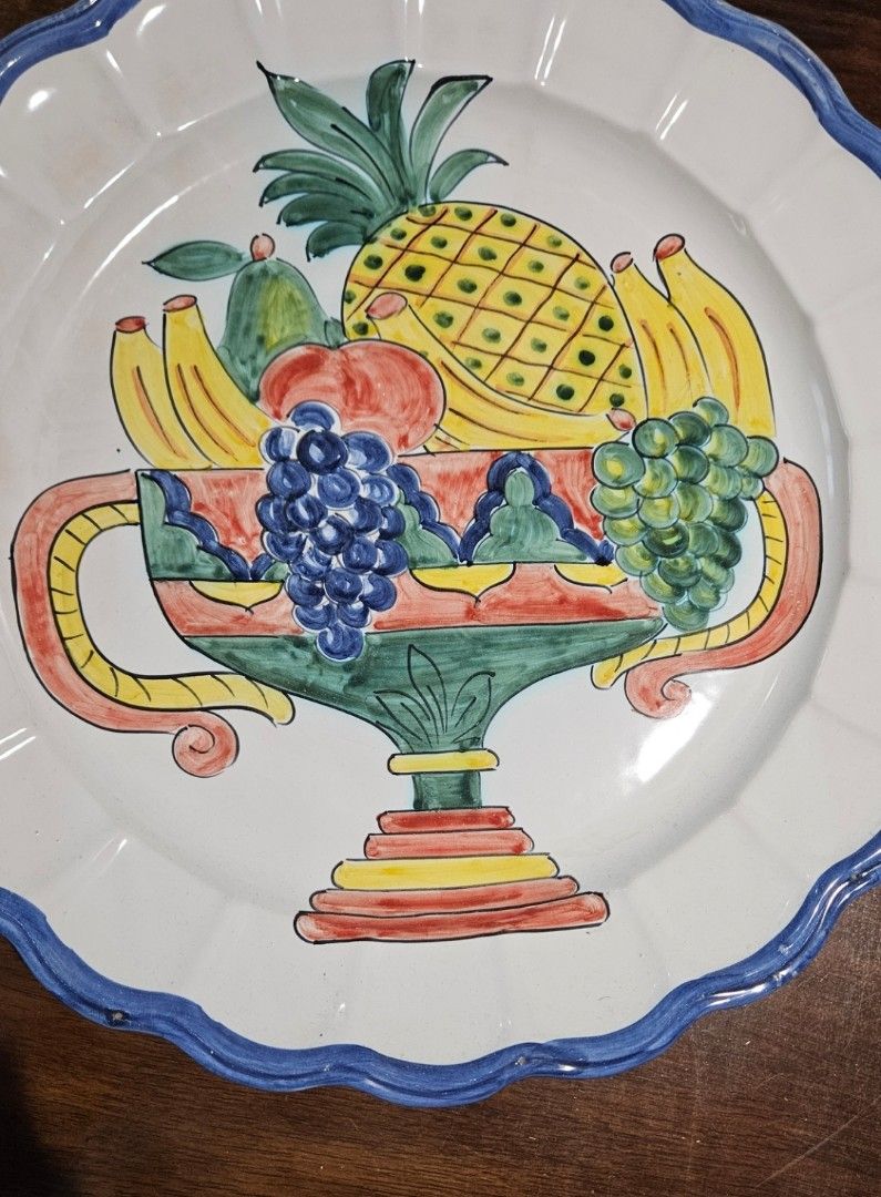 Hand-painted Italian style fruit decorative ceramic wall plate (Category: Wall Decor) located in Manila. Submitted by cosmicshark-cd31f1 (Listing ID 1470608086, Image 2). Description: - Large decorative ceramic plate with hand-painted fruit urn design (pineapple, grapes, bananas, pears) - Features a charming blue scalloped rim and vibrant glossy multi-color glaze - Signed signature on the back for authenticity - Built-in hanging holes on the ungl