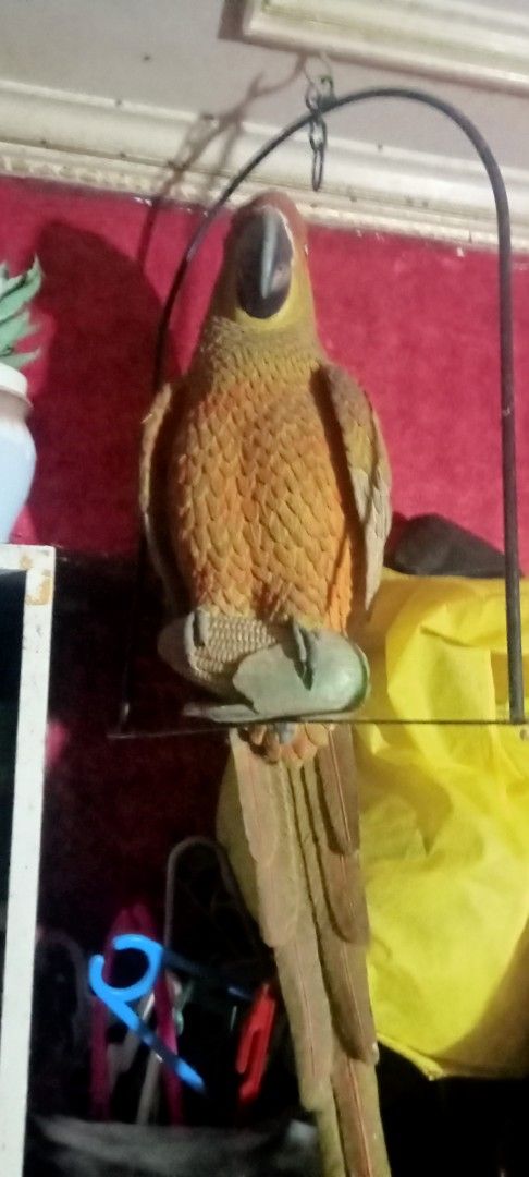 Hanging parrot statue with metal stand (Category: Figurines & Statues) located in Paranaque City. Submitted by dimaguilaa24827 (Listing ID 1470645868, Image 1). Description: - Textured parrot sculpture in rich brown and orange color tones - Complete with a sturdy metal hanging stand - Features intricate, detailed feather carvings all over the body - Designed with elegant long tail feathers hanging down - Unique decor piece perfect for indoor spac