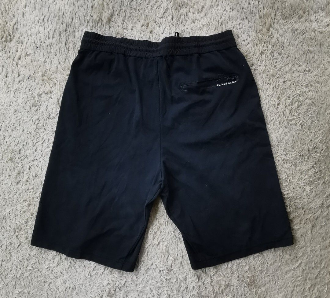 j.lindeberg Black Jersey Shorts with Drawstring Waist (Category: Shorts) located in Davao. Submitted by dmp1993 (Listing ID 1470622376, Image 2). Description: J.Lindeberg black shorts in jersey fabric. Elastic waistband with adjustable drawstring closure. Zippered back pocket featuring white text branding. Purple graphic patch attached near the lower hem. Clean dark finish overall, lightweight construction, suitable for training or casual wear..