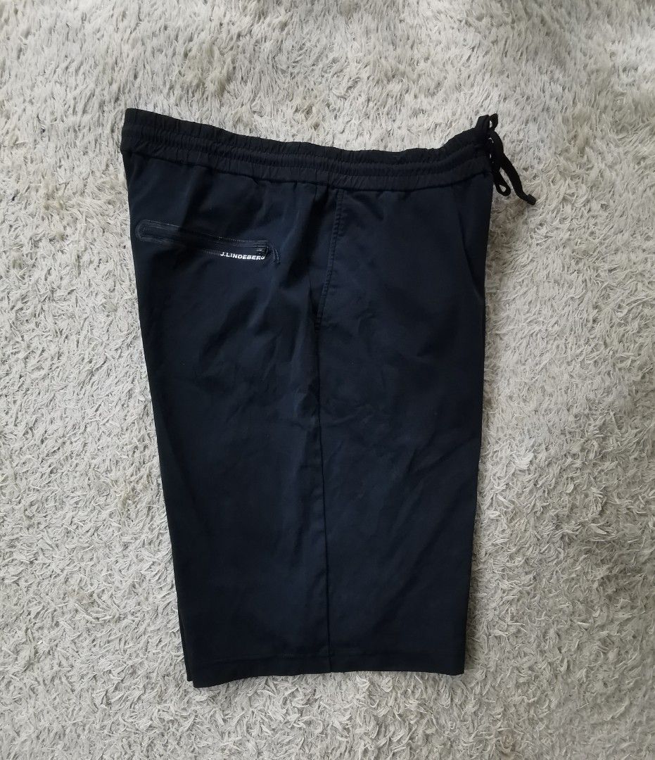 j.lindeberg Black Jersey Shorts with Drawstring Waist (Category: Shorts) located in Davao. Submitted by dmp1993 (Listing ID 1470622376, Image 3). Description: J.Lindeberg black shorts in jersey fabric. Elastic waistband with adjustable drawstring closure. Zippered back pocket featuring white text branding. Purple graphic patch attached near the lower hem. Clean dark finish overall, lightweight construction, suitable for training or casual wear..